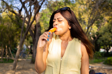 Happy young indian woman enjoying ice lolly or ice candy in hot summer day. Heat stroke.