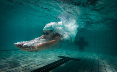 A talented female swimmer dives into a full-size tournament pool to train or compete. This stunning wide-angle underwater photo captures the grace and power of this athlete in action.