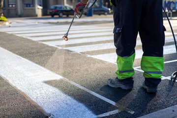 Process of making new road surface markings with a line striping machine, workers improve city infrastructure, demarcation marking of pedestrian crossing with a hot melted paint on asphalt pavement