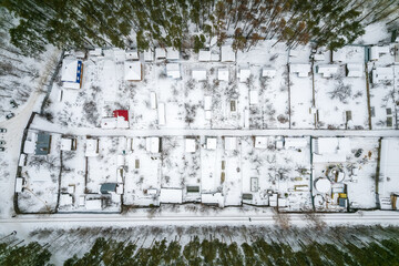 Aerial view of coniferous winter forest and a small houses.. Flying above frozen trees and snow...