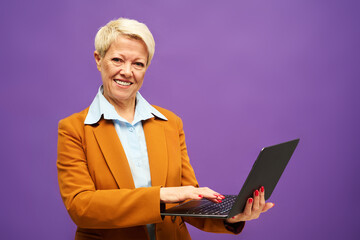 Happy mature businesswoman in formalwear looking at camera and looking through online data in...