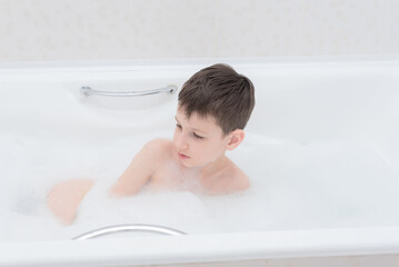 Happy boy takes a bath with lush foam playing with bubbles. Personal hygiene, healthcare concept