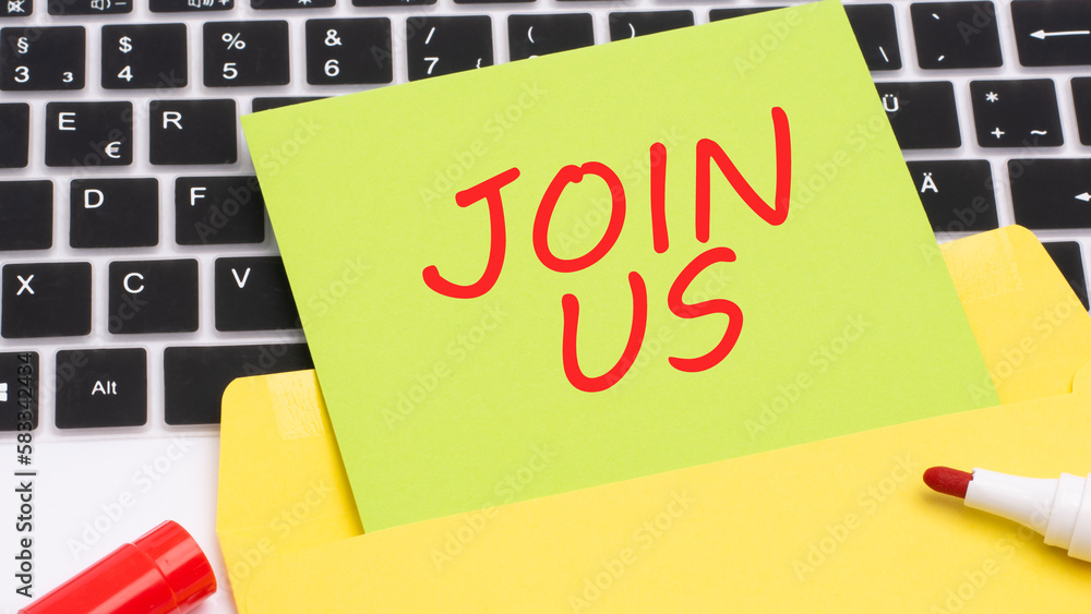 Poster text join us is written in red marker on a green card. in the frame is a laptop keyboard on yellow n