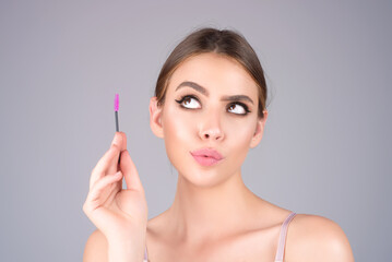 Beautiful woman applies brow gel with brows brush to her eyebrow. Studio portrait of young woman doing her eyebrow natural make up. Eyebrows make up concept.