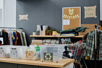 Part of spacious storage room or office of volunteering organization with plastic boxes for different types of garbage and second hand clothes