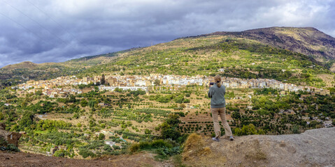 Young and blonde woman taking photos from a viewpoint to a town in the Alpujarra of Granada