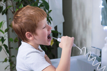 Boy brushes his teeth and oral cavity with irrigator in the bathroom. Hygiene and healthy lifestyle concept