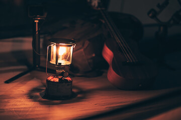 A gas lamp is on the tent floor at night and a bag with a ukulele and shoes next to it. Camping...