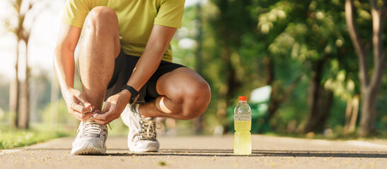 Young athlete man tying running shoes with Energy Drink water, male runner ready for jogging...