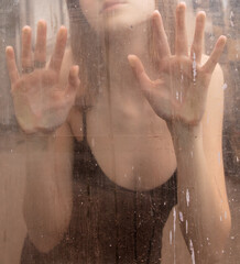 Girl's hands behind dirty glass
