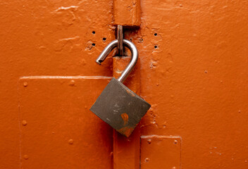 A metal padlock hangs on an orange door.