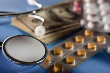 Fototapeta na wymiar Stack of American money with pills and stethoscope on blue background, closeup photo