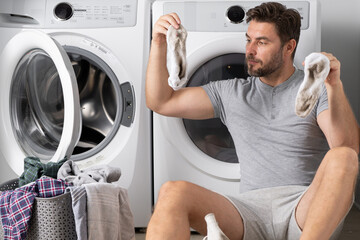 Portrait of sexy man with dirty clothes near washing machine. Handsome man sits in front of washing machine. Dirty laundry. Man cleaning clothes. Housework for single alone guy. Home laundry.