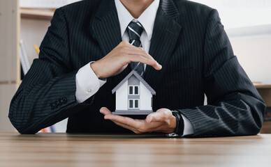 Concept of home and real estate Property insurance. Close up businessman of  hands sheltering modern house. .