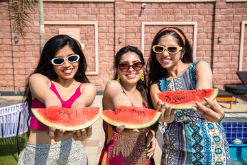 Three beautiful young indian girls having fun together and eating watermelon in hot summer day,...