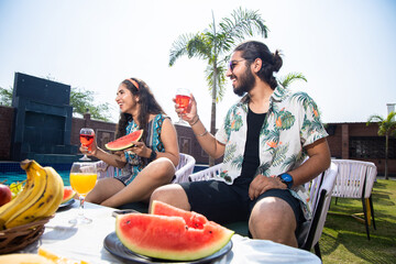 Happy indian friends enjoying watermelon together outdoor resort or hotel in sunny day, Young...