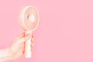 Female hand holding a small fan on pink background close-up. - obrazy, fototapety, plakaty