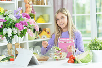 girl preparing fresh salad on kitchen table with tablet at home