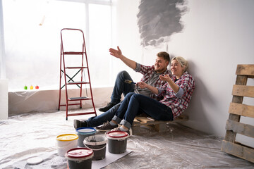 Young happy family married couple sitting on the floor dreams of renovating house and planning a design project