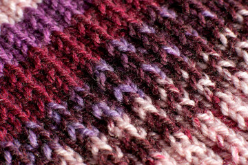 Knitted fabric close-up. Textural background in the form of a knitted pattern. Yarn for knitting in a linked product. Multi-colored stripes on a knitted fabric.