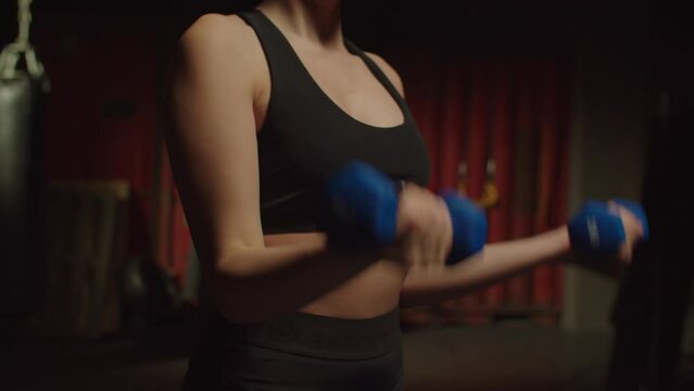 Midsection of determined sporty fit young woman doing weight training with dumbbells , performing bicep curls , strengthening arm and shoulder muscle in gym, Close-up.