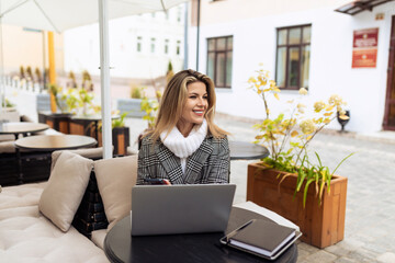 young european woman model in street cafe with laptop in spring