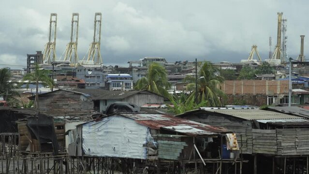 Wide shot of wooden stilt houses in the foreground. In the background are cranes at the port in Buenaventura, Colombia.
