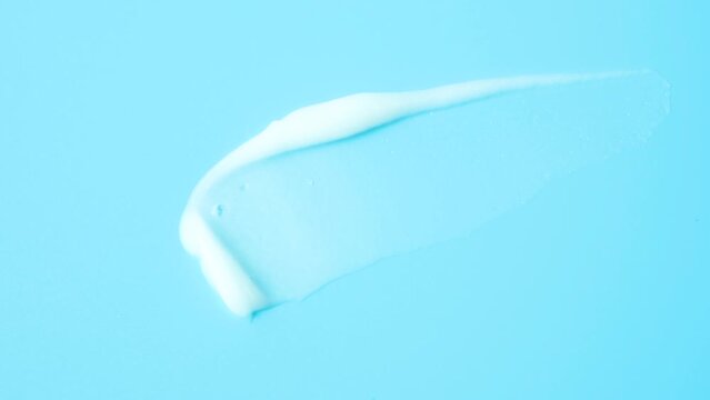 Smear of moisturizer moisturizing cream on blue background close-up, top view.