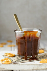 Salted caramel sauce dripping down the jar. Topping for cakes, pies, ice cream, cheesecakes. Salty pretzel cookies on a wooden serving board. High-calorie dessert. Close up