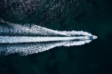 Big white boat with a blue awning fast movement on dark water top view.