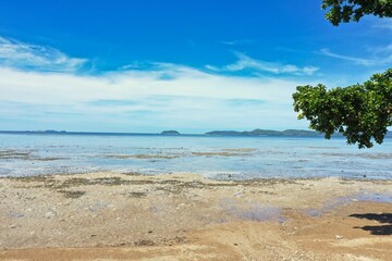 Sandy beach at low tide in Coron, Philippines, green hills and bright blue sky in the background.