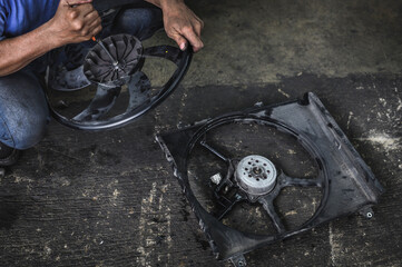 Auto mechanic uninstalling a radiator cooling fan from the radiator fans housing.