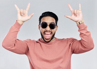 Portrait, rocker and hand gesture with a man in studio on a gray background feeling crazy or...