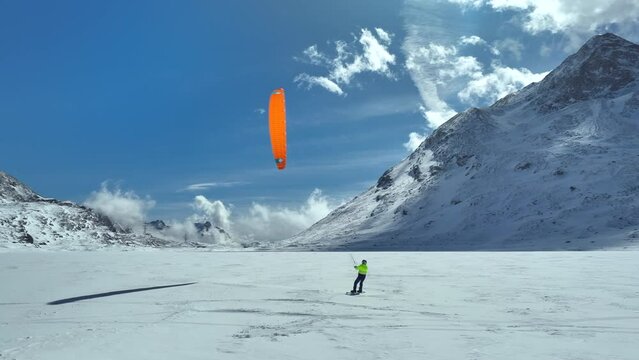 Snow kiter turning his orange kite on frozen lake in Switzerland in the afternoon sun. Droe panning shot