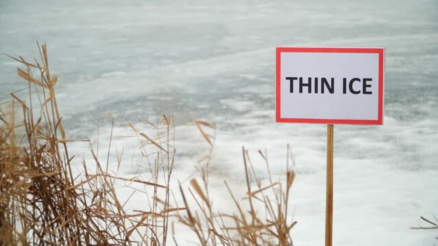 Close-up of a "Thin Ice" warning sign in front of a frozen lake. Stop, danger, warning.
