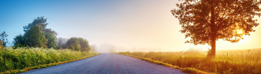 Sunrise in the foggy morning on the empty asphalt country road.