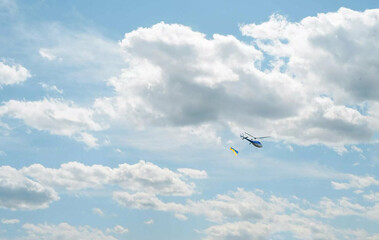 a helicopter with a Ukrainian flag is flying in the sky with clouds.