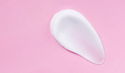 Face cream smear on pink background. White lotion swatch. Abstract cosmetic cream texture.
