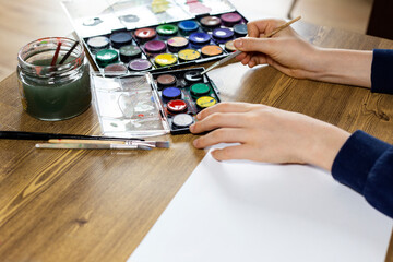 child creating drawing with multicolored paints and brush on wooden table close up