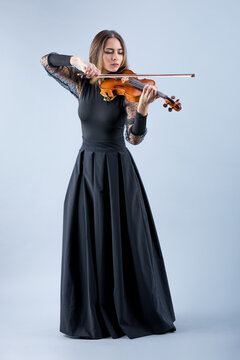 Violinist woman in the evening gown on the grey background.