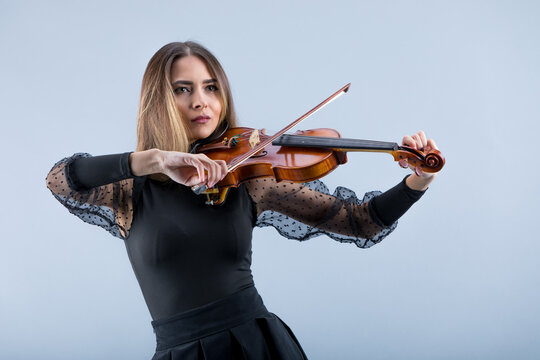 Violinist woman in the evening gown on the grey background.