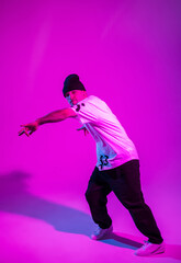 Fototapeta na wymiar Fashion professional breakdancer man dances in creative colored studio with pink and neon light