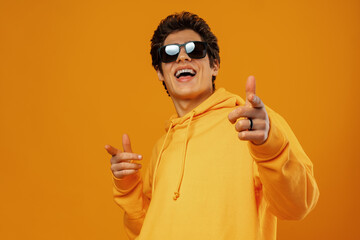 Handsome young man poses in sweatshirt and sunglasses on a yellow background