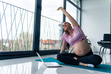 sporty pregnant woman sit on mat meditate practice yoga with online class on computer at home.