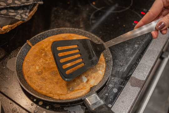 Woman cooking delicious thin pancakes on induction stove, closeup. A woman makes thin pancakes in a frying pan in the kitchen.