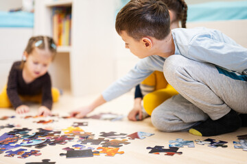 Children connecting jigsaw puzzle pieces in a kids room on floor at home.  Fun family activity leisure.