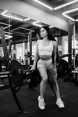 Fototapeta premium Young sporty girl in the gym resting after barbell exercises. Athletic body