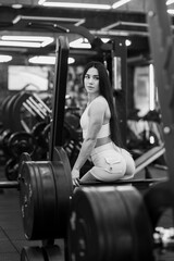 Young sporty girl in the gym resting after barbell exercises. Athletic body