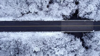 Top down aerial pan along country road by snowy winter forest in USA - Powered by Adobe