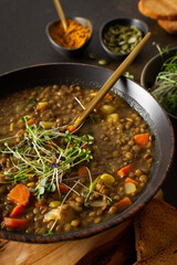 Healthy vegetarian lunches, brown lentil soup with tomatoes and carrots, potatoes and curry spices, toasted croutons, bowl with soup on cutting board on brown background